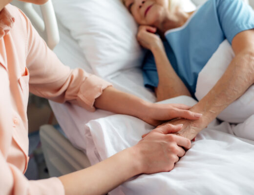 Eine Angehörige hält die Hand einer Frau im Krankenbett.